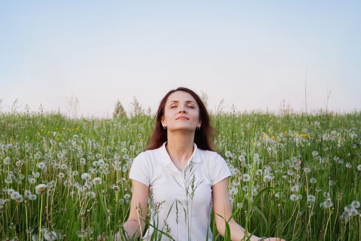 A woman sits in a green field with her eyes closed, breathing slowly.