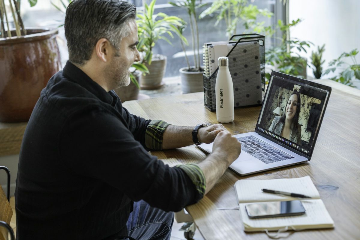 A man at a sunny desk talks with a counselor on a video call.